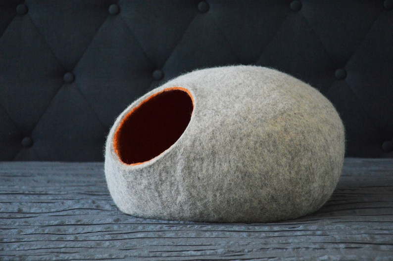 May include: A gray felt cat bed shaped like a cave with an orange felt opening.