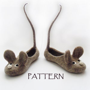 Puede incluir: Un par de pantuflas de ratón de fieltro gris con colas largas. Las pantuflas tienen ojos negros y narices blancas.