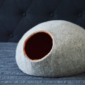 May include: A gray felt cat bed shaped like a dome with an orange felt trim around the entrance hole.