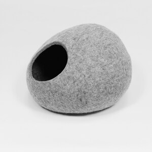May include: A gray felt cat bed shaped like a rounded oval with a large opening on the side.