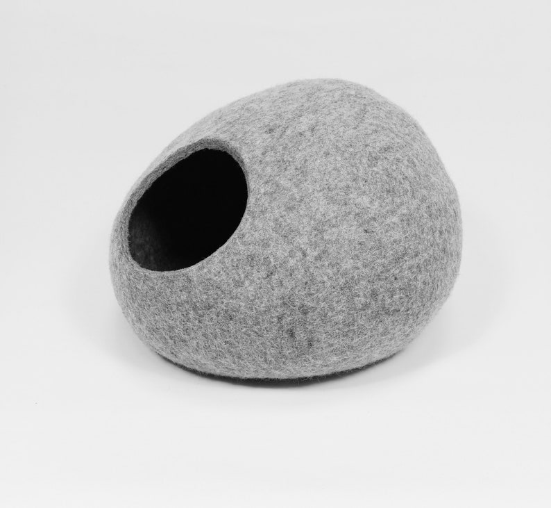 May include: A gray felt cat bed shaped like a rounded oval with a large opening on the side.