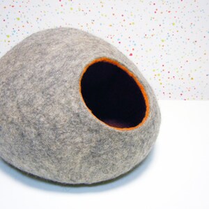 May include: A gray felt cat bed shaped like an egg with an orange felt trim around the entrance.