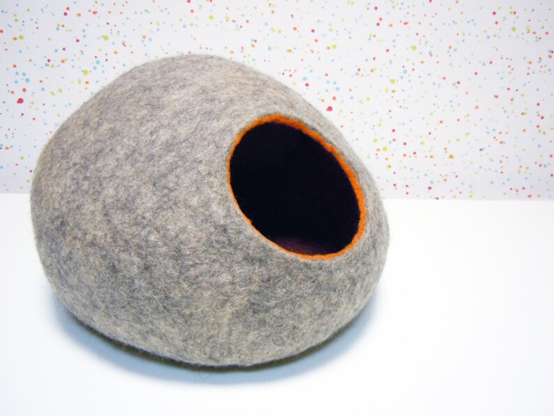 May include: A gray felt cat bed shaped like an egg with an orange felt trim around the entrance.