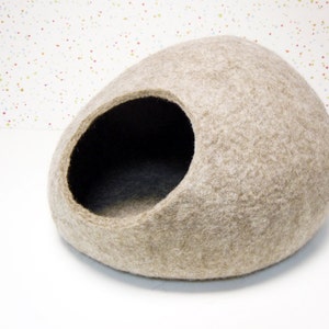 Pode incluir: Uma cama para gatos de feltro bege em forma de oval arredondado com uma grande abertura lateral. A cama &eacute; feita de materiais naturais e fornece um espa&ccedil;o aconchegante e confort&aacute;vel para os gatos dormirem e relaxarem.