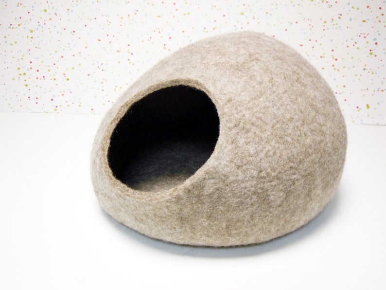 Pode incluir: Uma cama para gatos de feltro bege em forma de oval arredondado com uma grande abertura lateral. A cama &eacute; feita de materiais naturais e fornece um espa&ccedil;o aconchegante e confort&aacute;vel para os gatos dormirem e relaxarem.