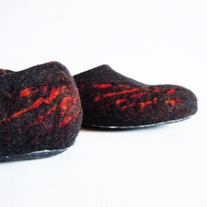 May include: A pair of black felt slippers with vibrant red abstract designs. The slippers have a rounded toe and a low profile, suitable for indoor wear. The felt material provides a soft and comfortable feel.