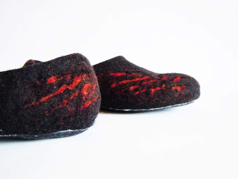 May include: A pair of black felt slippers with vibrant red abstract designs. The slippers have a rounded toe and a low profile, suitable for indoor wear. The felt material provides a soft and comfortable feel.