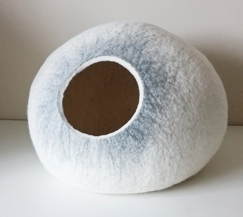 May include: A white and gray felted cat bed shaped like a sphere with a round opening.