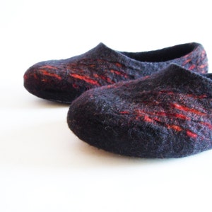 May include: A pair of dark blue felt slippers with vibrant red streaks. These cozy, handmade slippers have a rounded toe and a low-profile design, perfect for indoor wear. The felted wool provides warmth and comfort.