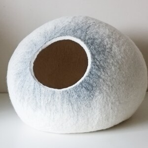 May include: A white and gray felt cat bed shaped like a sphere with a round opening.