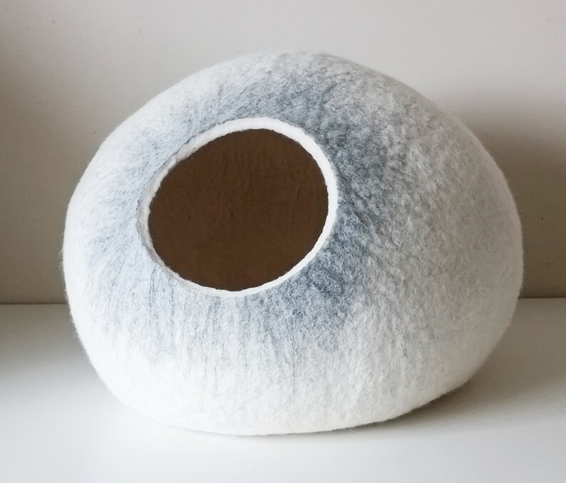 May include: A white and gray felt cat bed shaped like a sphere with a round opening.