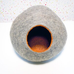 May include: A gray felt cat bed shaped like a dome with an orange felt interior.