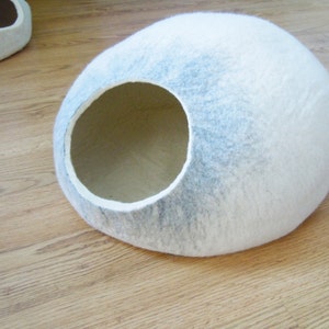 May include: A white and gray felt cat bed shaped like a dome with a round entrance hole.
