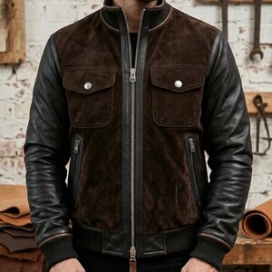 Puede incluir: Chaqueta bomber de ante marrón y cuero negro. La chaqueta tiene una cremallera frontal, dos bolsillos en el pecho con cierres de botón a presión plateados y dos bolsillos laterales con cremallera. Las mangas son de cuero negro.