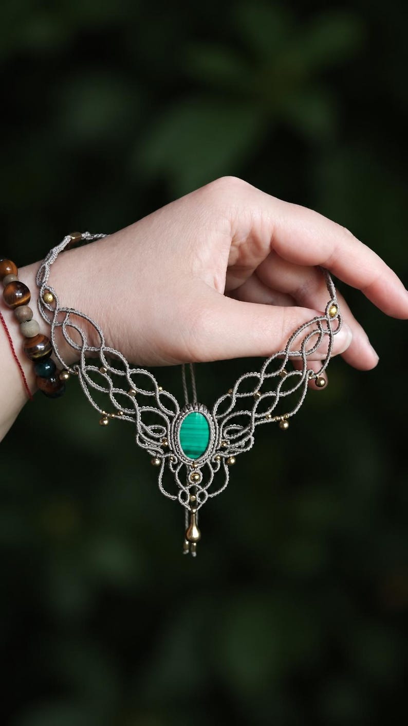 Peut inclure: Un collier en macram&eacute; avec une pierre centrale ovale en malachite verte aux motifs ray&eacute;s. Le collier est r&eacute;alis&eacute; en cordon marron clair avec un design nou&eacute; complexe, agr&eacute;ment&eacute; de petites perles dor&eacute;es et d'une breloque couleur or.