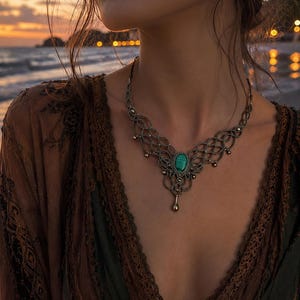 Peut inclure: Un collier compos&eacute; d'une pierre ovale centrale en malachite verte sertie dans une monture en fil m&eacute;tallique sombre avec des motifs en treillis complexes et de petites perles m&eacute;talliques pendantes, attach&eacute; &agrave; une cha&icirc;ne en m&eacute;tal sombre.