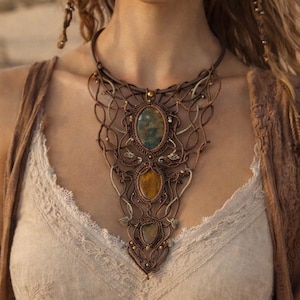 Puede incluir: Un collar de macramé marrón con tres piedras preciosas ovaladas en tonos verdes y amarillos. El collar tiene un cordón de cuero y detalles intrincados tejidos, creando un estilo bohemio.