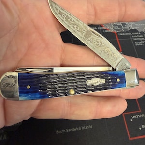 May include: A white ceramic mug with a black handle and the text "But First, Coffee" in a black, handwritten-style font. The mug is on a white surface.