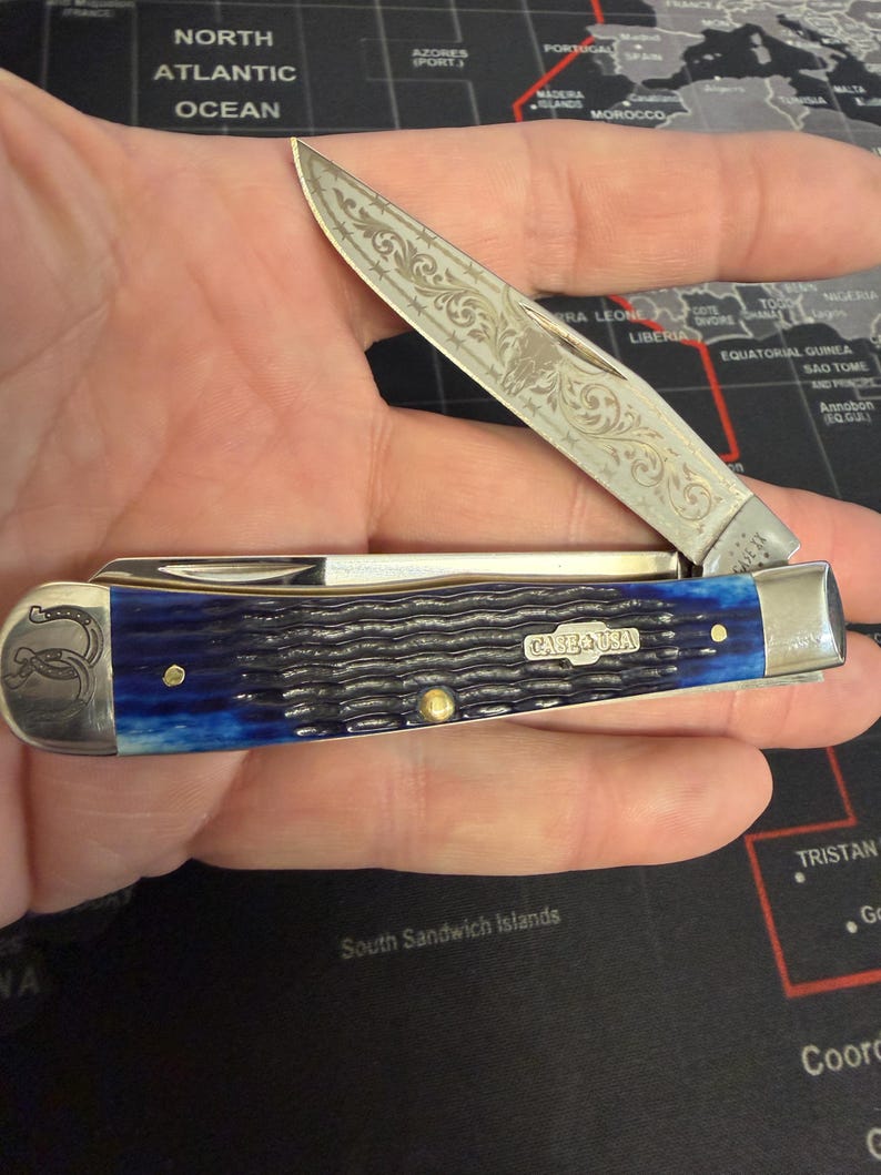 May include: A white ceramic mug with a black handle and the text "But First, Coffee" in a black, handwritten-style font. The mug is on a white surface.