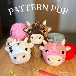 May include: A collection of handmade crochet cow heads in various colors, including white, brown, and pink, with black accents. The image includes balls of yarn and a crochet hook. The text "PATTERN PDF" is displayed at the top.