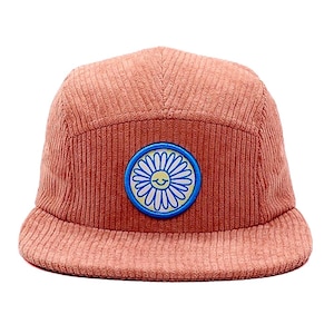May include: A coral corduroy cap with a flat peak. The cap has a circular patch with a blue border, a yellow centre, and a smiling daisy design. The hat has a five-panel design.