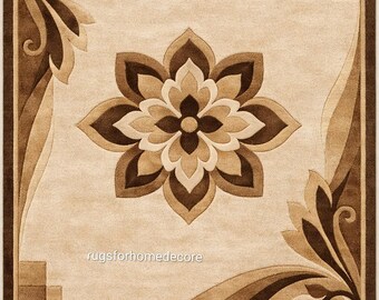 May include: Beige and brown floral patterned area rug. The rug features a large flower in the centre, surrounded by curved lines and decorative corner elements. The text "rugsforhomedecore" is visible near the bottom.
