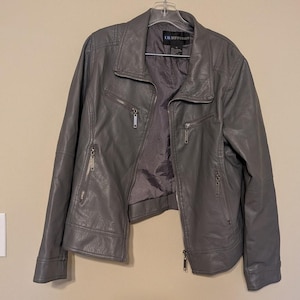 May include: A grey jacket with a collared neckline, long sleeves, and a front zipper closure. The jacket features two diagonal zippered pockets on the chest and two lower zippered pockets. A label inside the neck reads LB DIFFUSION.