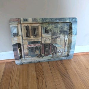 May include: A rectangular serving tray featuring a printed illustration of a Parisian street scene with multi-story buildings, storefronts labeled Commerce Vins and Cafe Paris, open windows, and outdoor cafe tables with chairs under a tree.