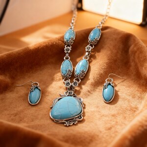 May include: A silver-toned necklace and earring set featuring turquoise-colored stones. The necklace has a large, irregular-shaped pendant and smaller oval stones. The earrings mirror the oval stone design. Floral accents adorn the metalwork.