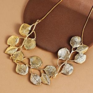 May include: A gold-colored necklace featuring a leaf design. The necklace has multiple leaf-shaped pendants connected by delicate chains. The leaves have a textured surface, and the necklace is displayed on a neutral background.
