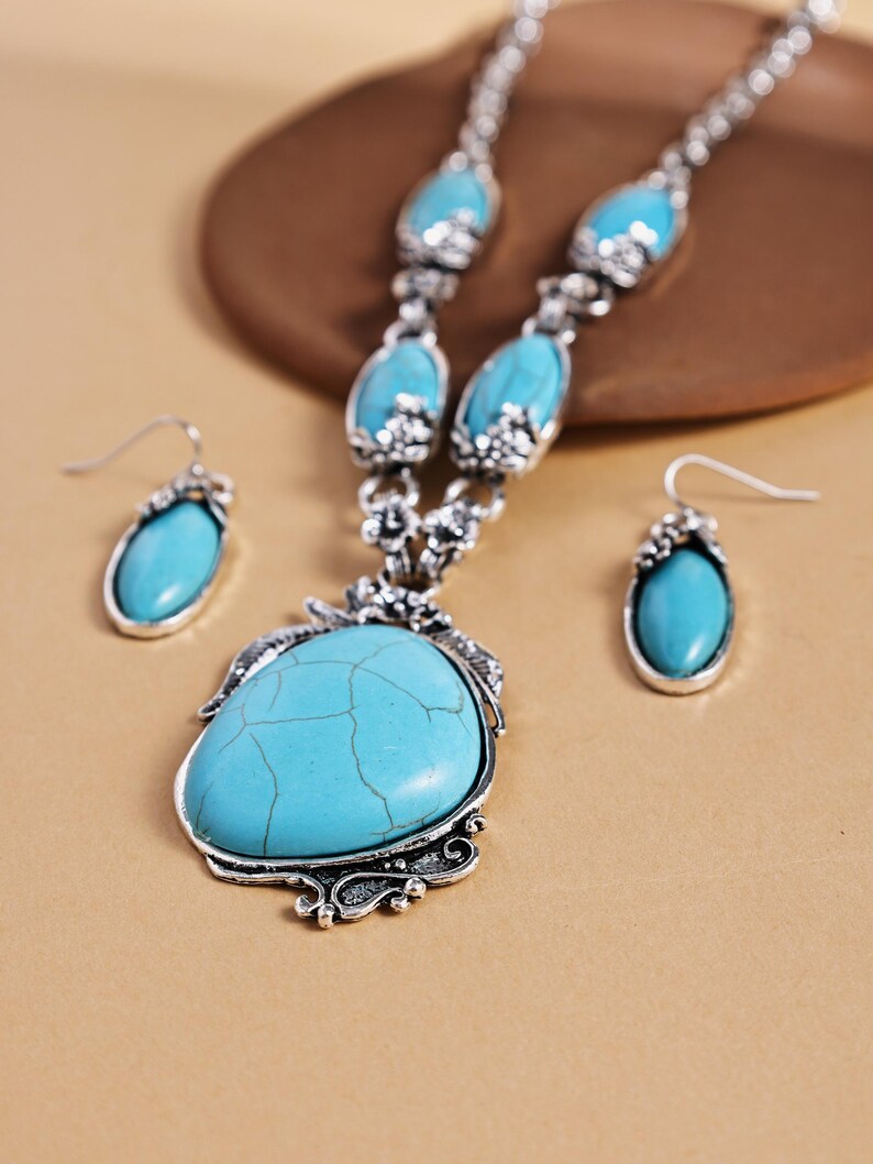 May include: A turquoise jewelry set featuring a necklace and matching earrings. The necklace has a large, teardrop-shaped turquoise pendant with a silver-colored filigree setting. The earrings mirror the pendant's shape. The set is displayed on a neutral background.