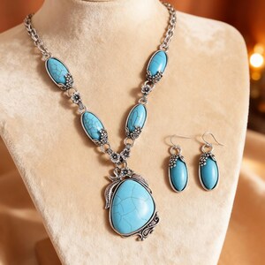 May include: A silver-toned necklace and earring set featuring turquoise-colored oval and teardrop-shaped stones. The necklace has a large pendant and smaller stones along the chain. The earrings match the necklace design.