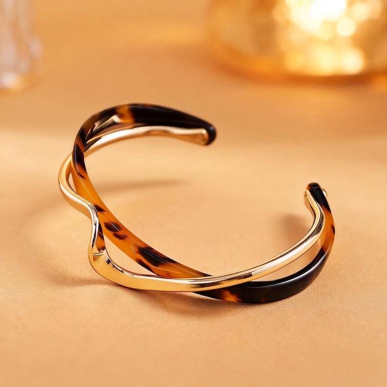 Peut inclure: Un bracelet manchette dor&eacute; avec un motif &eacute;caille de tortue. Le bracelet ouvert pr&eacute;sente un design tourbillonnant avec une finition polie. Les sections en &eacute;caille de tortue sont marron et noir.