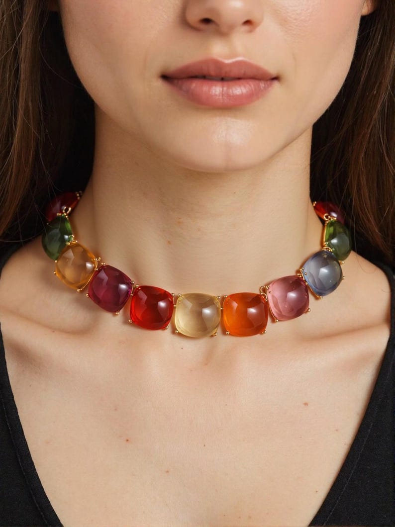 May include: A colorful necklace featuring large, square-cut gemstones in a variety of colors, including red, orange, yellow, pink, green, and purple. The gemstones are set in gold-colored metal. The necklace is a statement piece.