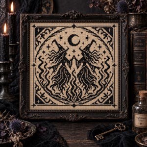 May include: A square cross-stitch embroidery featuring a black design on a beige fabric background. The pattern depicts two figures in pointed hats, a crescent moon, and stars, all enclosed within a decorative black frame with ornate edges.