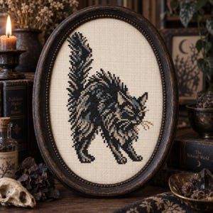 May include: An oval-framed cross-stitch embroidery featuring a stylized, arched-back cat in shades of black, charcoal, and cream. The cat is depicted with long, textured fur and a raised tail, centered on a light beige fabric within a dark wood frame.