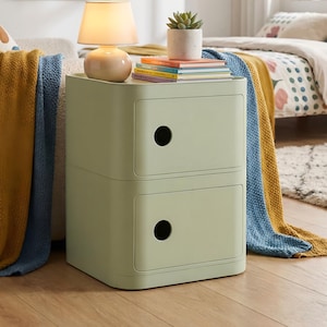 May include: A pale green bedside cabinet with two drawers and a rounded design. A small beige lamp, a succulent in a white pot, and books are on top. A yellow and blue blanket is draped over a sofa.