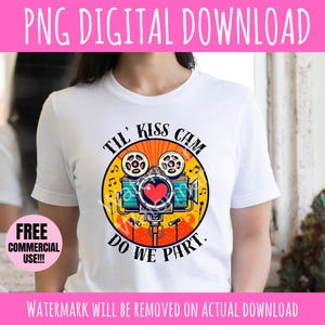 May include: White t-shirt featuring a colorful graphic of a vintage movie camera with a heart in the center. The text on the shirt reads "Til' Kiss Cam Do We Part." The design includes musical notes and a retro style.