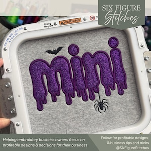 May include: A grey fabric piece secured in a white embroidery hoop featuring the purple glittery text mini in a dripping font style. The design includes a small black embroidered bat above the text and a black spider hanging from the letter i.