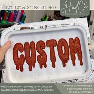 May include: A white embroidery hoop containing a fabric piece with the word CUSTOM stitched in a dripping, glittery orange font. The hoop frame features warning labels, and the text 12, 10 & 8 INCLUDED is visible at the top of the image.