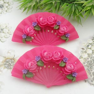 Puede incluir: Dos pinzas para el pelo de plástico rosa en forma de abanico con detalles florales en relieve. Las flores son rosas, blancas y verdes.