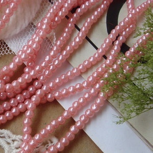 May include: A strand of pink pearl beads. The beads are small and round, and they are strung together on a clear thread.