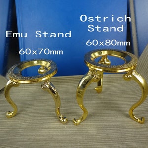 May include: Two ornate, gold-coloured stands. The left stand is labelled "Emu Stand" and measures 60 x 70mm. The right stand is labelled "Ostrich Stand" and measures 60 x 80mm. Both stands have a decorative, circular top and curved legs.