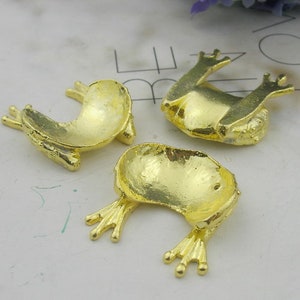 May include: Three gold frog figurines. Each frog is in a different pose. The frogs are small and would be great for adding a touch of whimsy to a craft project.