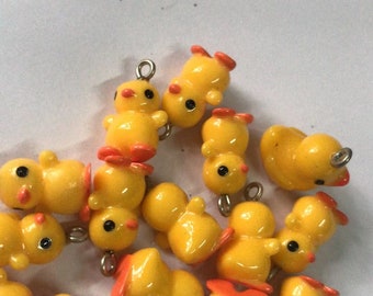 May include: A group of yellow rubber duck charms with orange beaks and black eyes. The charms have silver jump rings for attaching to jewellery or other crafts.