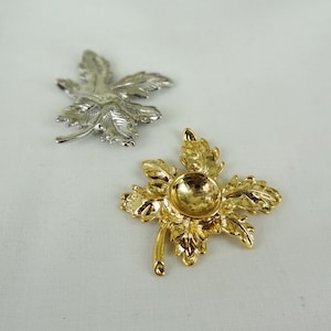 May include: Two metal leaf-shaped ornaments. One is gold and has a round centre. The other is silver and has a more detailed design.