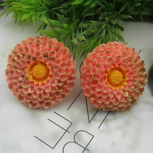 Puede incluir: Dos pendientes en forma de flor de color rosa y dorado con centros amarillos.