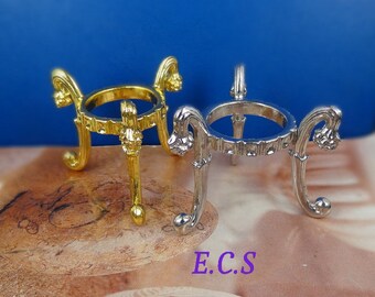 May include: Two decorative metal stands for displaying spheres. The stand on the left is gold and the stand on the right is silver. Both stands have a round top and three legs with ornate details.