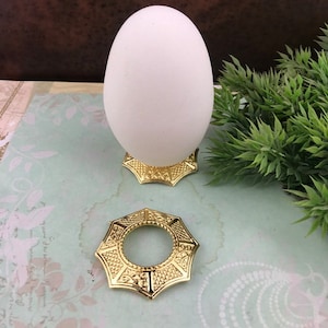 Könnte beinhalten: Goldener Eierhalter aus Metall mit dekorativem Design. Der Halter hat eine runde Oberseite und eine sternförmige Basis. Der Halter ist leer.