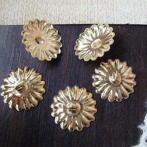 May include: Five gold-coloured metal flower-shaped embellishments with a raised centre. The embellishments have a scalloped edge and a hole in the centre.